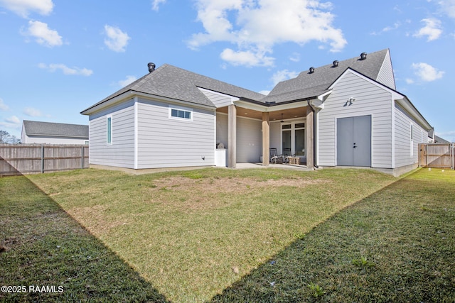 back of property with a shingled roof, a fenced backyard, a lawn, and a patio