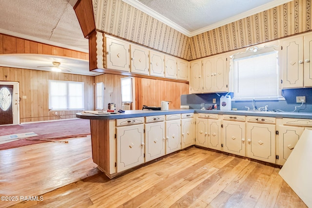 kitchen featuring a textured ceiling, light wood-style flooring, crown molding, a peninsula, and wallpapered walls