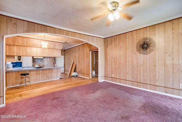 unfurnished living room featuring arched walkways, carpet, crown molding, a textured ceiling, and ceiling fan with notable chandelier