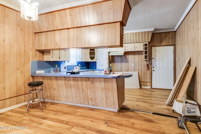 kitchen with open shelves, ornamental molding, light wood-style floors, wooden walls, and a peninsula