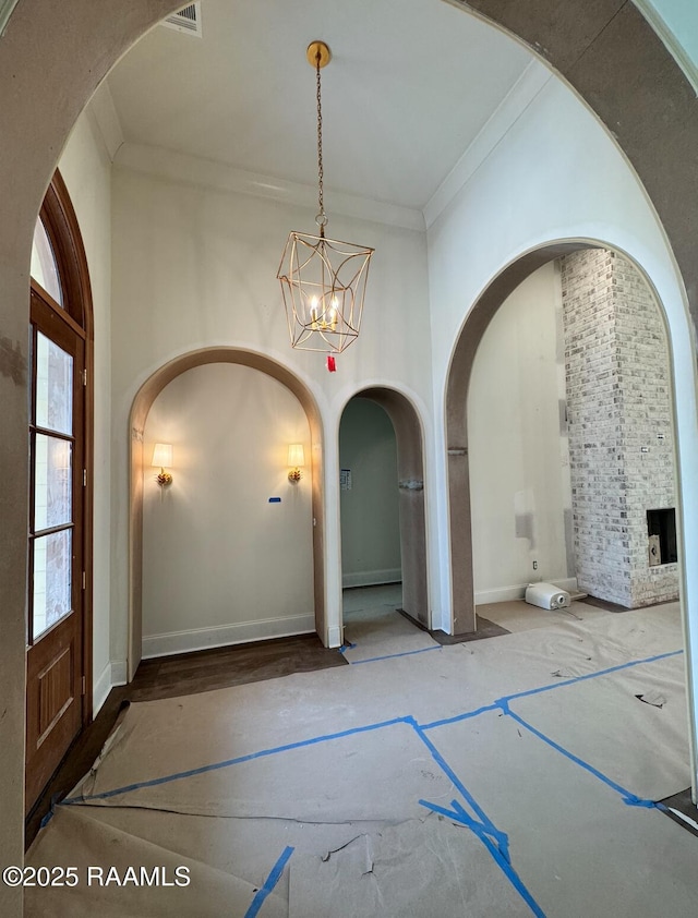 entryway with baseboards, arched walkways, a towering ceiling, ornamental molding, and an inviting chandelier