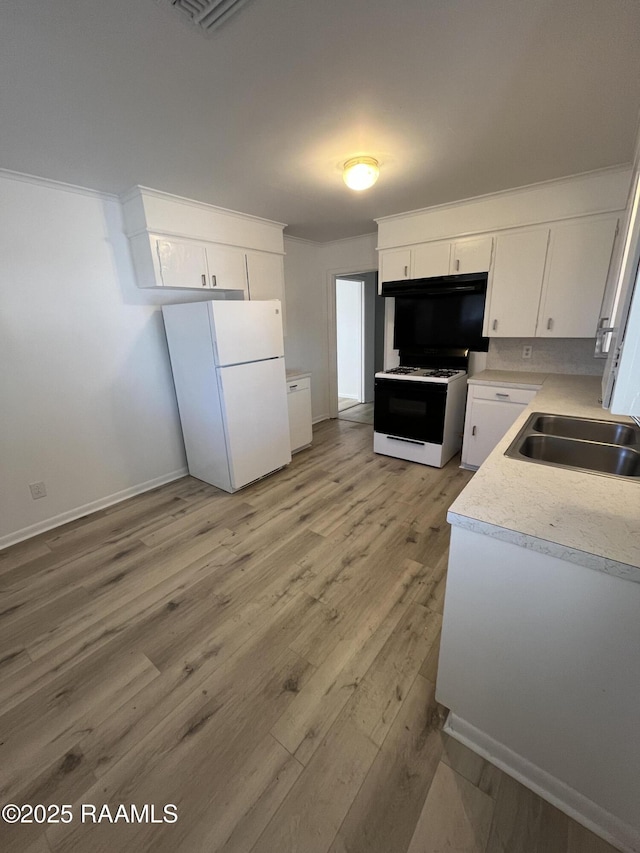 kitchen with light countertops, freestanding refrigerator, white cabinetry, a sink, and gas range