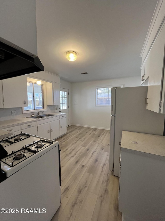 kitchen with white appliances, white cabinets, light wood-style flooring, light countertops, and a sink