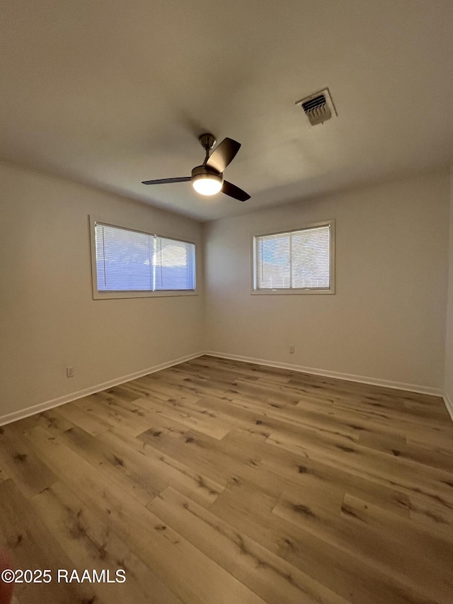 spare room with a ceiling fan, wood finished floors, visible vents, and baseboards