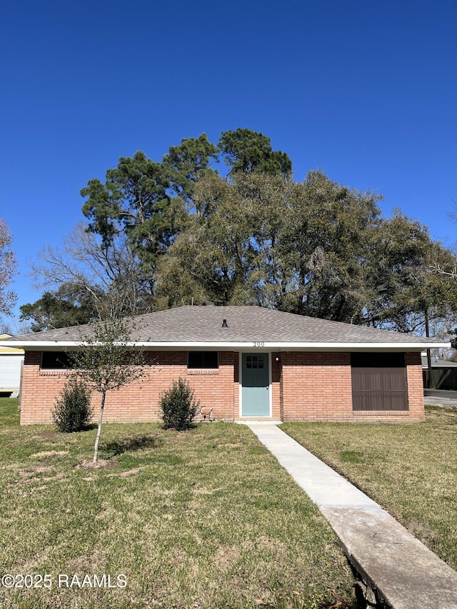 view of front of home featuring brick siding, roof with shingles, and a front yard