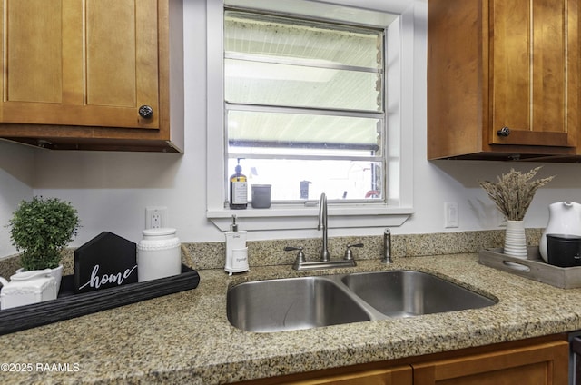 kitchen featuring brown cabinetry, a sink, and light stone countertops