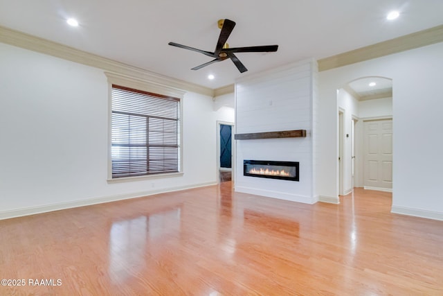 unfurnished living room featuring light wood-style floors, a fireplace, ornamental molding, and arched walkways