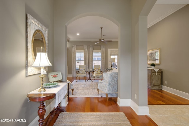 sitting room with baseboards, arched walkways, a ceiling fan, wood finished floors, and crown molding