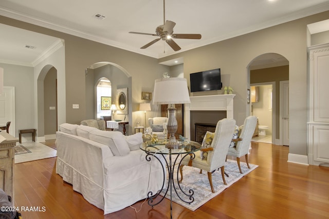 living room featuring baseboards, visible vents, wood finished floors, crown molding, and a fireplace