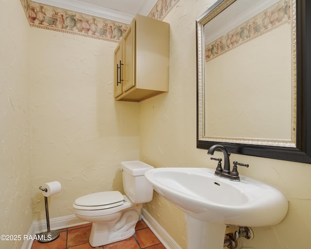 half bath featuring a textured wall, toilet, a sink, baseboards, and tile patterned floors