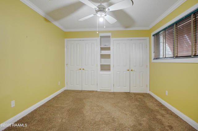 unfurnished bedroom with carpet floors, baseboards, ornamental molding, and two closets