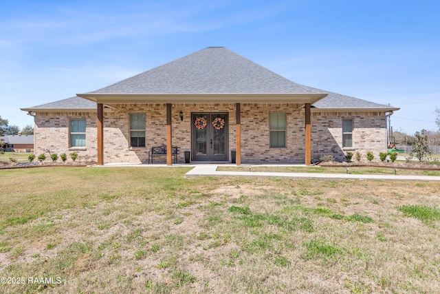 view of front of property with roof with shingles, a front lawn, french doors, and brick siding