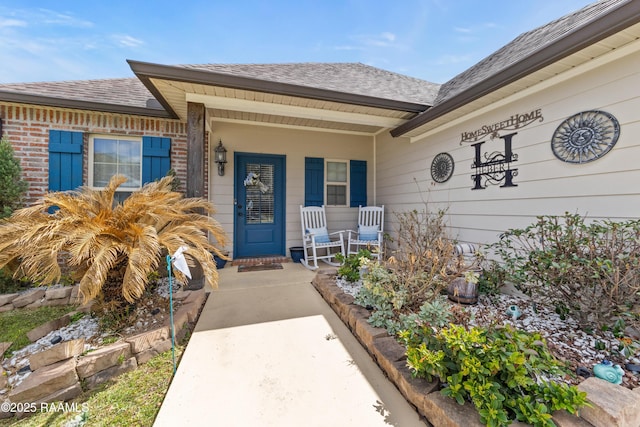 property entrance with brick siding, covered porch, and roof with shingles