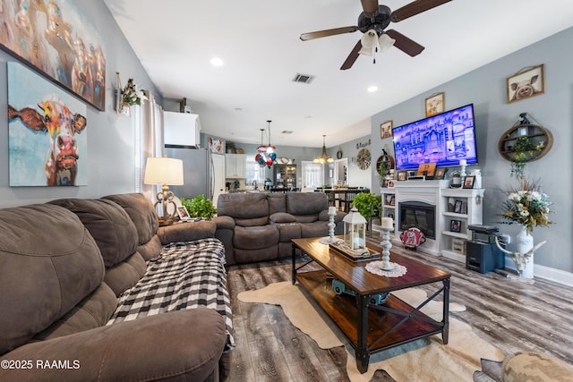 living area with wood finished floors, visible vents, baseboards, recessed lighting, and a glass covered fireplace