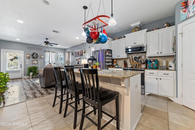 kitchen featuring tasteful backsplash, a center island, light tile patterned floors, stainless steel appliances, and white cabinetry