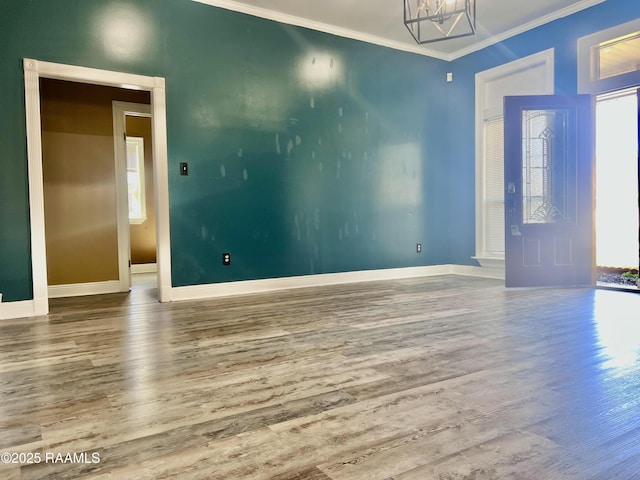 empty room with a chandelier, ornamental molding, wood finished floors, and baseboards