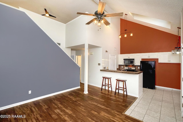 kitchen with a peninsula, a ceiling fan, white cabinetry, appliances with stainless steel finishes, and dark countertops