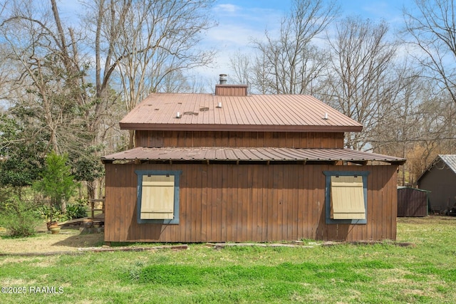 view of property exterior with metal roof, a yard, a chimney, and an outbuilding