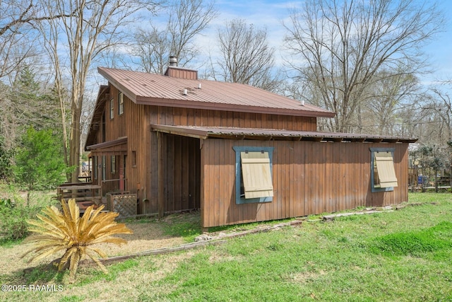 view of home's exterior with a chimney, metal roof, and a yard