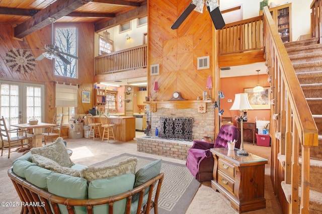 living room with wooden walls, wood ceiling, visible vents, stairs, and a ceiling fan