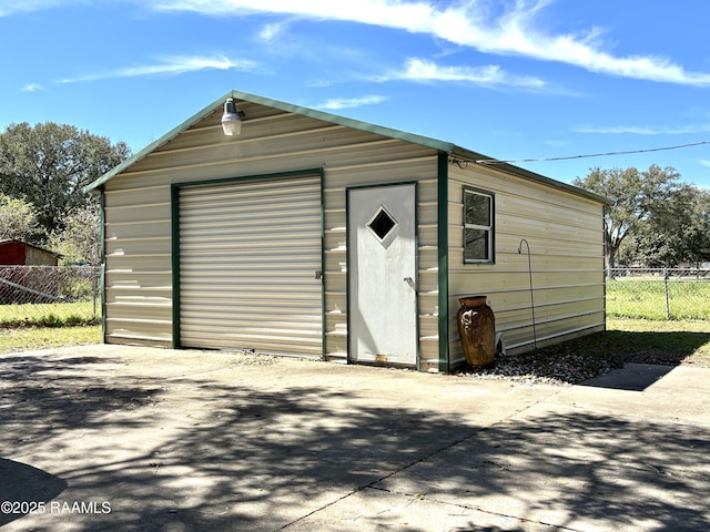 view of outdoor structure with driveway, fence, and an outbuilding