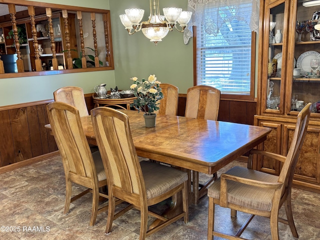 dining room with wood walls, stone finish flooring, and a notable chandelier