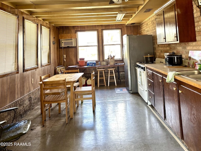 kitchen featuring gas range gas stove, light countertops, an AC wall unit, wood walls, and a sink