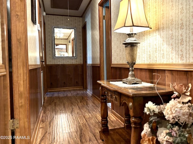 interior space with a wainscoted wall, dark wood finished floors, attic access, ornamental molding, and wallpapered walls