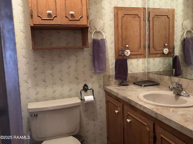 half bathroom with vanity, toilet, and wallpapered walls