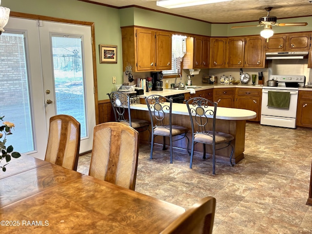 kitchen with electric stove, a breakfast bar area, light countertops, wainscoting, and under cabinet range hood