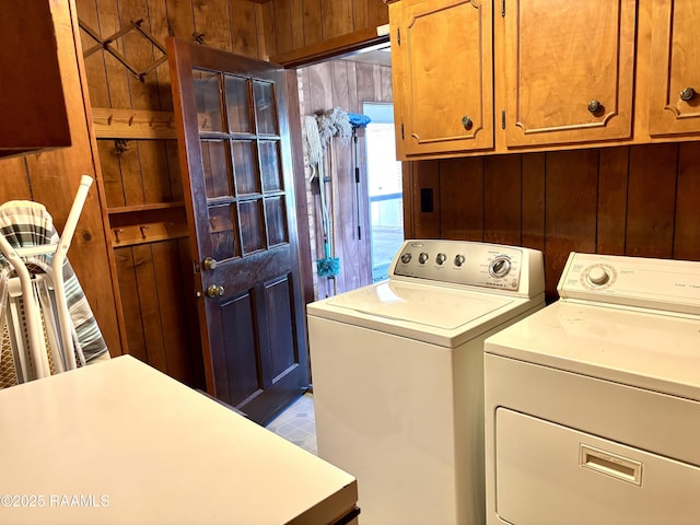 washroom with cabinet space, wood walls, and washing machine and clothes dryer