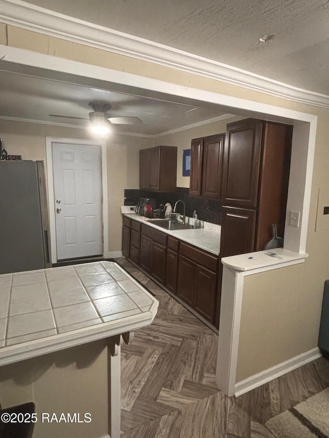 kitchen featuring parquet floors, crown molding, freestanding refrigerator, a sink, and dark brown cabinets