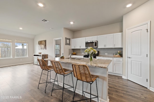 kitchen with a breakfast bar area, tasteful backsplash, stainless steel microwave, visible vents, and black gas stove