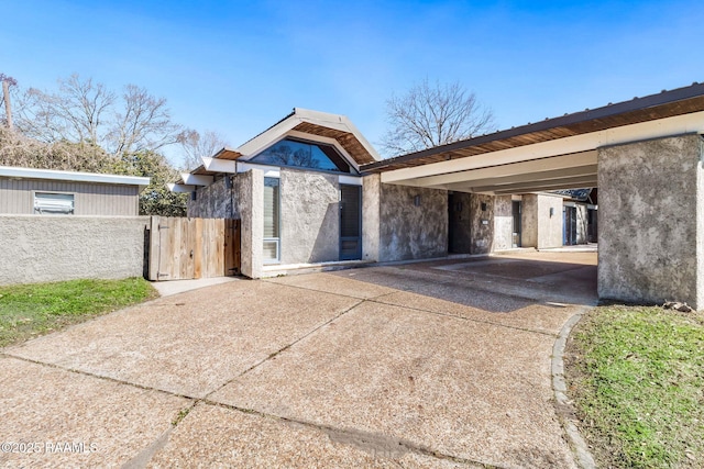 view of front of property with an attached carport, concrete driveway, fence, and stucco siding