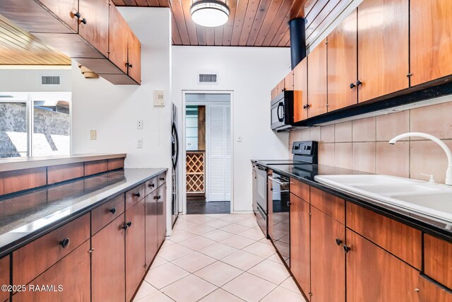 kitchen featuring light tile patterned floors, tasteful backsplash, visible vents, a sink, and black appliances