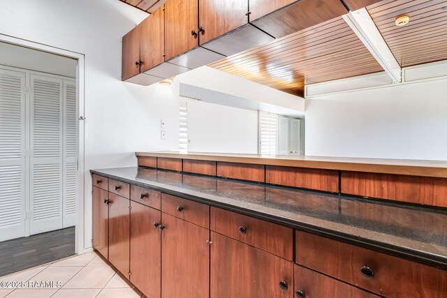 kitchen with brown cabinets, dark countertops, wood ceiling, and light tile patterned flooring