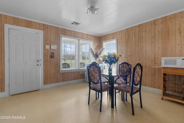 dining space with visible vents, wood walls, crown molding, and baseboards