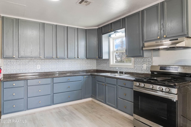 kitchen featuring stainless steel gas range oven, under cabinet range hood, a sink, visible vents, and light wood-style floors