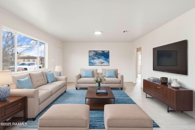 living area with light wood-style flooring, visible vents, and ornamental molding