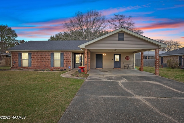 view of front of home with driveway, a carport, a yard, roof with shingles, and brick siding