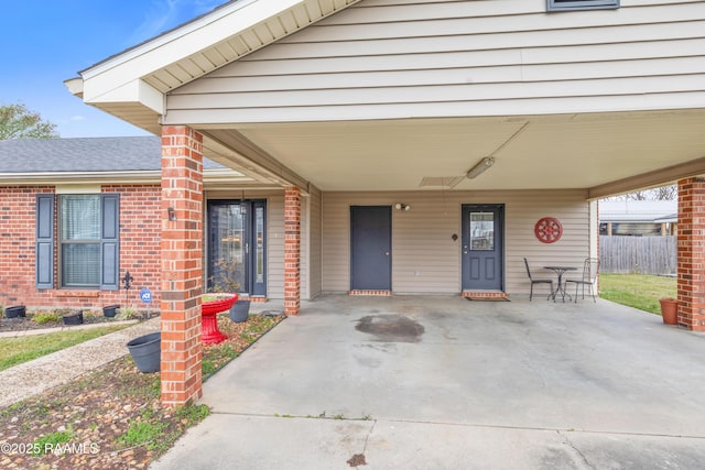 doorway to property featuring a carport, fence, and a shingled roof