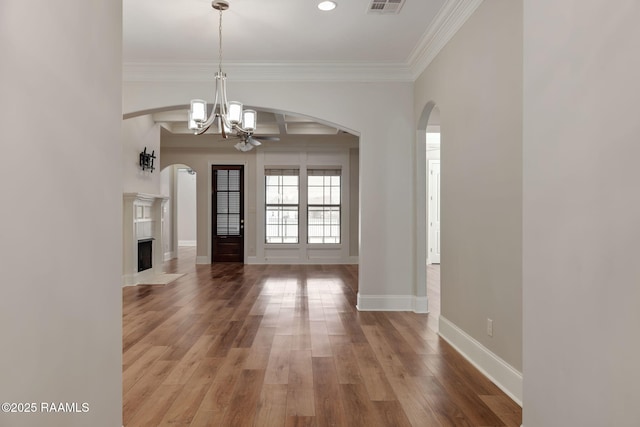 interior space with baseboards, arched walkways, wood finished floors, crown molding, and a fireplace