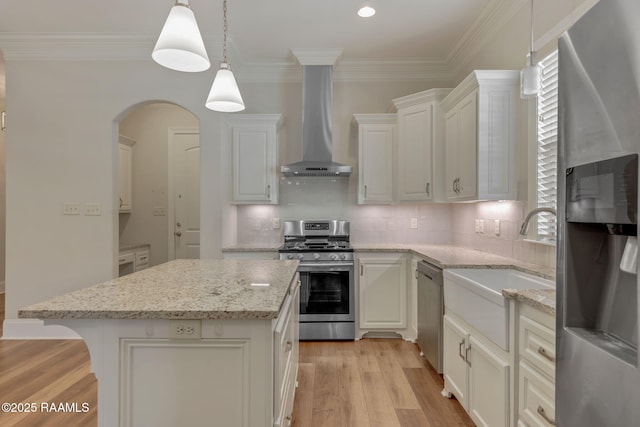 kitchen featuring a kitchen island, light wood-style floors, appliances with stainless steel finishes, wall chimney exhaust hood, and crown molding