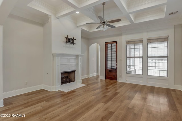 unfurnished living room featuring visible vents, arched walkways, a premium fireplace, light wood-style floors, and beam ceiling