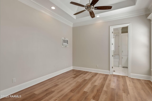 spare room with ornamental molding, a tray ceiling, light wood-style flooring, and baseboards