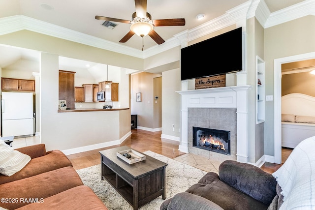 living area with baseboards, visible vents, a ceiling fan, a tiled fireplace, and vaulted ceiling