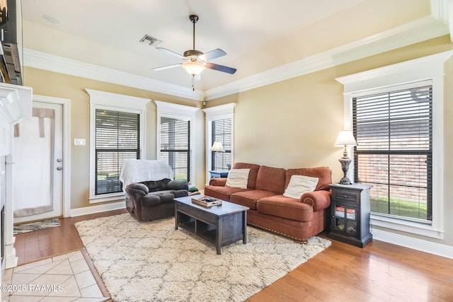 living area with ceiling fan, visible vents, baseboards, light wood-style floors, and ornamental molding