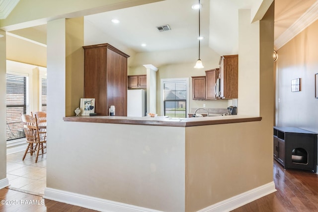 kitchen with brown cabinetry, freestanding refrigerator, visible vents, and wood finished floors