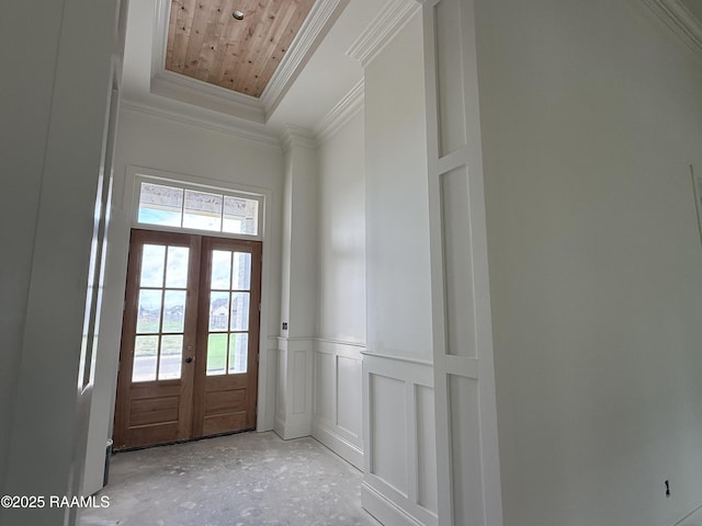 doorway with a tray ceiling, french doors, crown molding, a decorative wall, and wainscoting