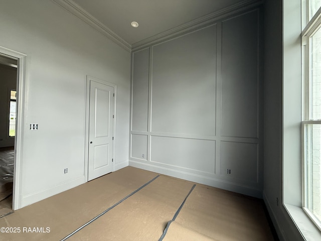 empty room featuring a healthy amount of sunlight, baseboards, ornamental molding, and a decorative wall